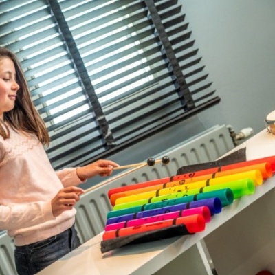 Instrumento musical colorido em tubos sobre mesa com criança a tocar numa sala com janela