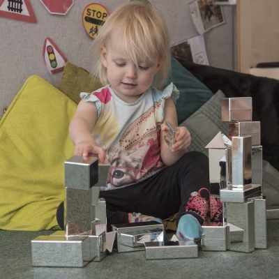 Criança a brincar com blocos de construção prateados em diferentes formas geométricas no chão