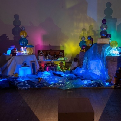 Decoração com esferas coloridas e tecidos brilhantes iluminados por luzes LED numa sala com chão de madeira