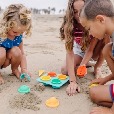 Crianças brincando na praia com formas de areia coloridas de plástico.