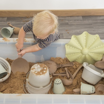 Criança a brincar com areia e acessórios de brincar em caixa plástica