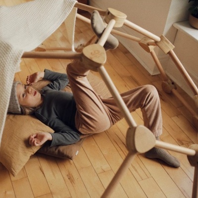 Estrutura de madeira clara para criança com criança deitada em almofada castanha no chão de madeira