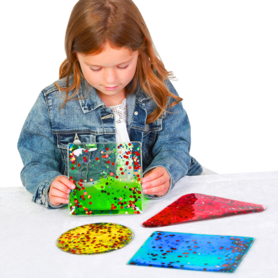Criança segurando peça transparente verde com confetes coloridos, com peças geométricas coloridas no tampo branco