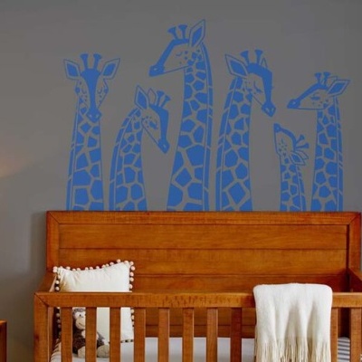 Paredes cinza com decalques azuis de girafas sobre berço de madeira clara e lâmpada branca