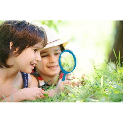 Duas crianças a observarem relva com uma lupa azul num ambiente exterior