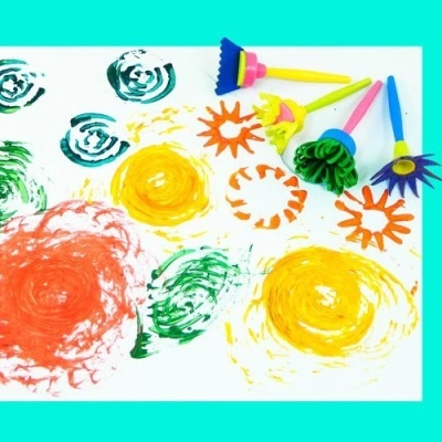 Carimbos de espuma coloridos com padrões florais e espirais sobre fundo branco e azul.