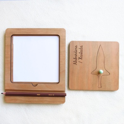 Dois tabuleiros quadrados de madeira com desenho de adaga e papel branco, acompanhados de dois lápis