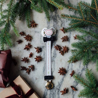 Prenda de Natal em forma de chupeta com laço e sineta rodeada de ramos de pinheiro e anis-estrelado com caixas de presente.