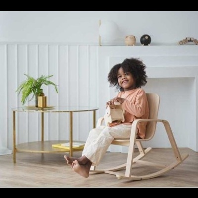 Criança numa cadeira de baloiço de madeira clara em sala moderna com mesa de vidro e planta