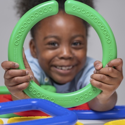 Criança segurando brinquedo plástico verde circular com texturas em relevo.