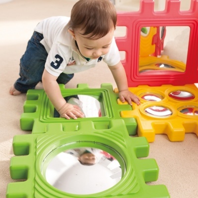Brinquedo infantil com peças coloridas e espelhos no chão com criança a brincar