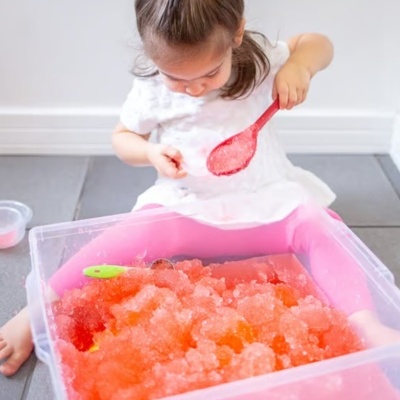 Criança brincando com gelo colorido em caixa plástica