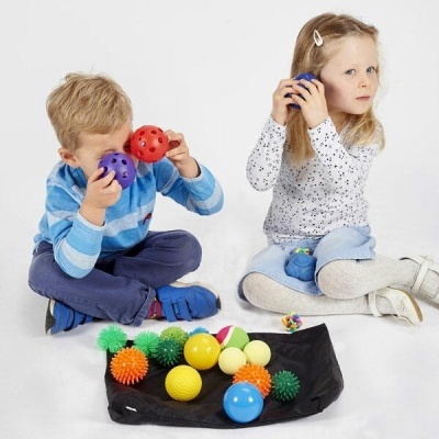 Crianças sentadas com várias bolas coloridas e diferentes texturas ao redor