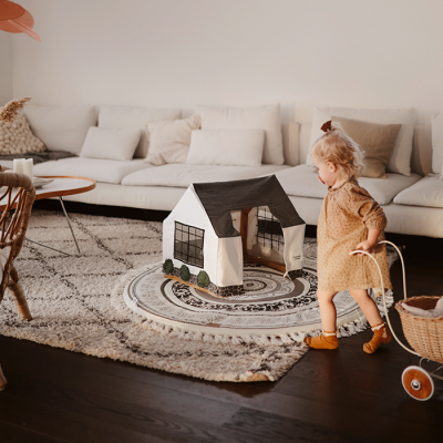 Tenda de brincar preta e branca sobre tapete redondo com criança e sofá ao fundo