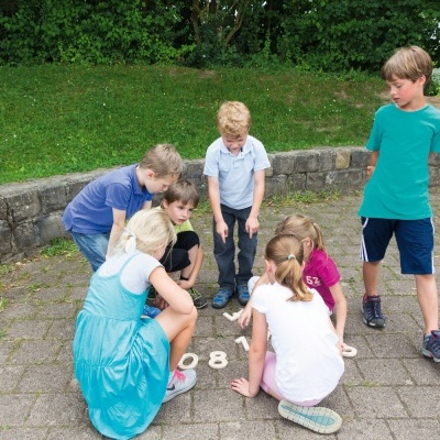 Crianças a observar números pintados no chão num parque