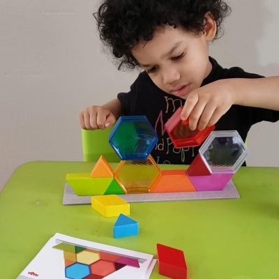 Criança a montar blocos geométricos coloridos translúcidos numa mesa verde