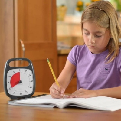 Relógio de tempo de cozinha e menina a escrever num caderno numa mesa de madeira
