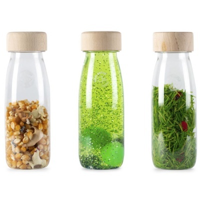 Três frascos transparentes com tampas de madeira contendo sementes, líquido verde com esferas e ervas verdes.