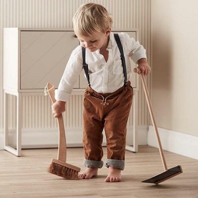 Criança com roupa vintage segurando vassoura e pá pequena em chão de madeira