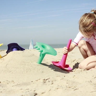 Cinco pás coloridas de plástico e criança a brincar na areia da praia.