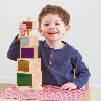 Criança sorridente a brincar com brinquedo de empilhar de madeira colorido em cima de mesa com toalha xadrez vermelha