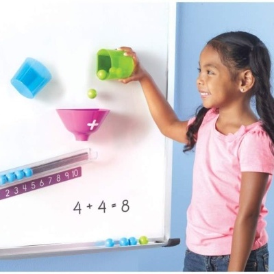 Menina com camisa rosa derrama bolas verdes em funil rosa no quadro branco com régua numérica e equação 4 + 4 = 8