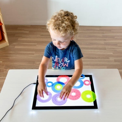 Tablet ou painel LED com formas circulares coloridas e criança a tocar