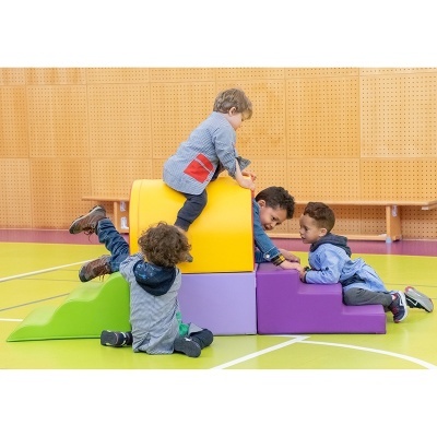 Crianças a brincar com blocos de espuma coloridos em ginásio.