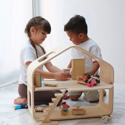 Duas crianças a brincar com casa de bonecas de madeira clara com móveis e acessórios coloridos
