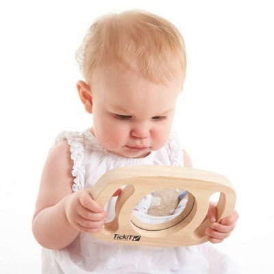 Bebé com vestido branco a segurar brinquedo de madeira com espelho redondo