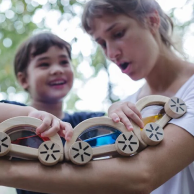 Mulher e criança brincando com brinquedo de madeira com janelas coloridas ao ar livre
