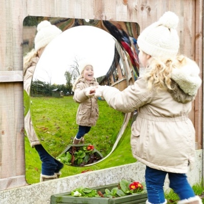 Criança refletida num espelho convexo quadrado instalado numa vedação de madeira