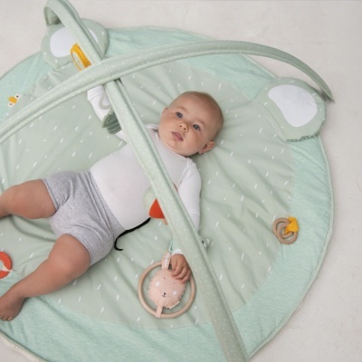 Bebé deitado num tapete redondo verde claro com três brinquedos pendurados