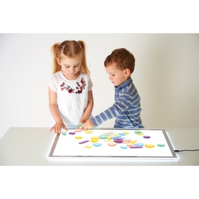 Duas crianças a brincar com objetos coloridos numa mesa iluminada branca