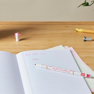 Caneta branca e rosa sobre caderno aberto com texto em tinta rosa numa mesa de madeira clara