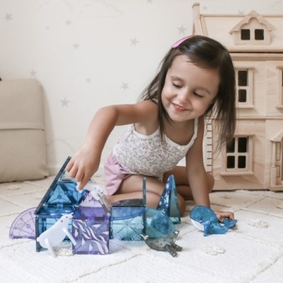 Menina brincando com blocos magnéticos translúcidos azuis e roxos no chão.