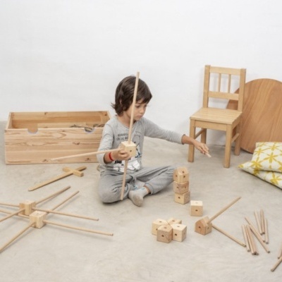 Criança a brincar com blocos e varas de madeira num ambiente minimalista com cadeira e almofada