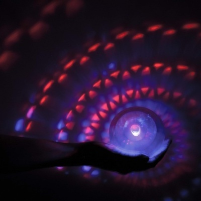 Mão segurando esfera de cristal com luzes projetadas coloridas