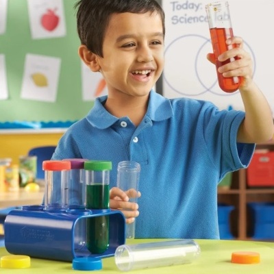 Criança numa sala de aula segurando tubo de ensaio com líquido vermelho