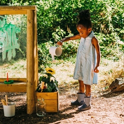 Menina regando planta junto a quadro negro em ambiente natural