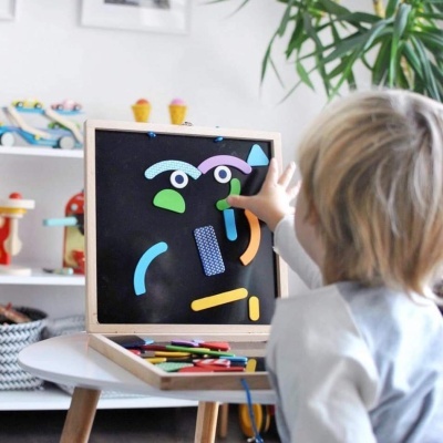 Criança a brincar com quadro magnético de madeira e peças coloridas