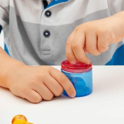 Criança com camisa cinza e branca segurando frasco azul com tampa vermelha