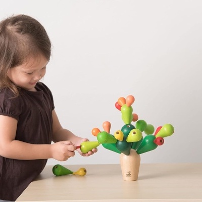 Criança a brincar com brinquedo de madeira em forma de cacto colorido numa mesa clara