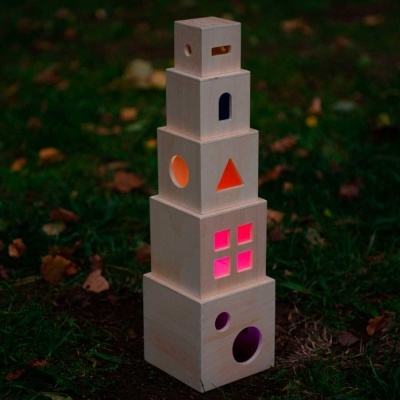 Torre de madeira clara com janelas iluminadas a cores em relva