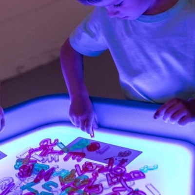 Criança usando mesa luminosa com letras e números coloridos de plástico