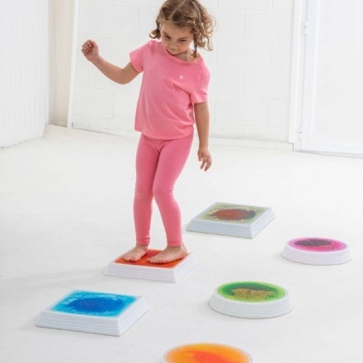 Criança sobre plataformas coloridas brancas em chão branco