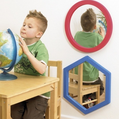 Criança com globo terrestre azul junto a mesa de madeira com espelhos coloridos na parede