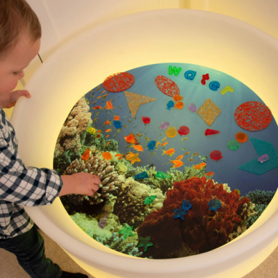 Criança junto a mesa iluminada com imagem subaquática e letras coloridas