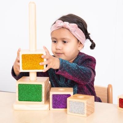 Criança empilhando blocos de madeira coloridos com glitter em mesa clara