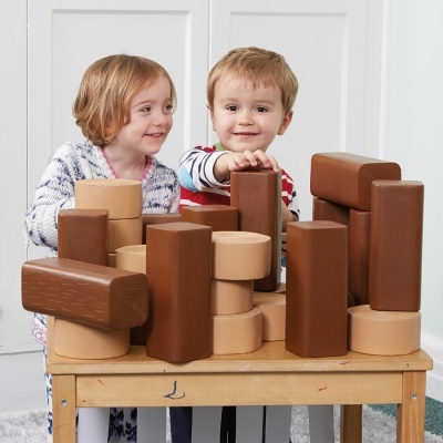 Criança e menina brincam com blocos de construção de madeira em tons castanhos numa mesa
